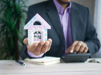 man holding model house at desk with calculator